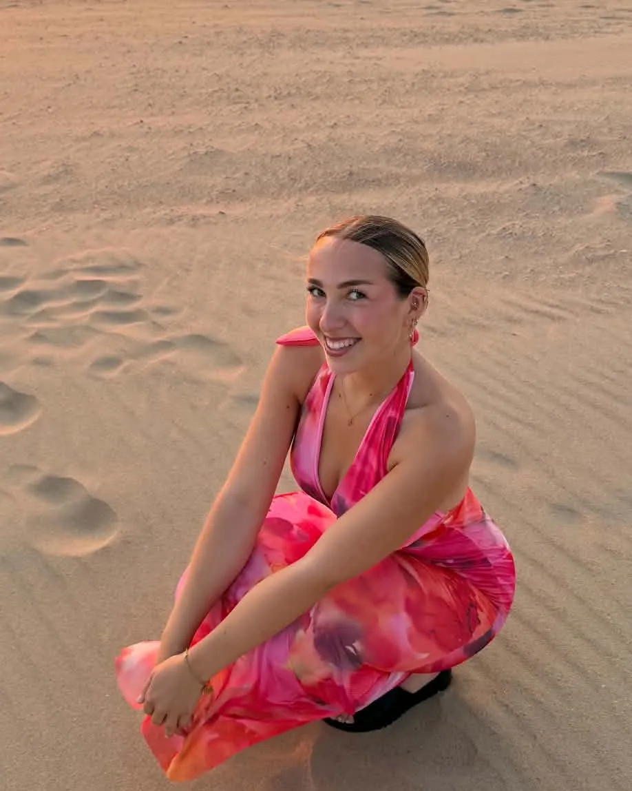 Louise accroupie sur une plage au coucher du soleil, en robe rose